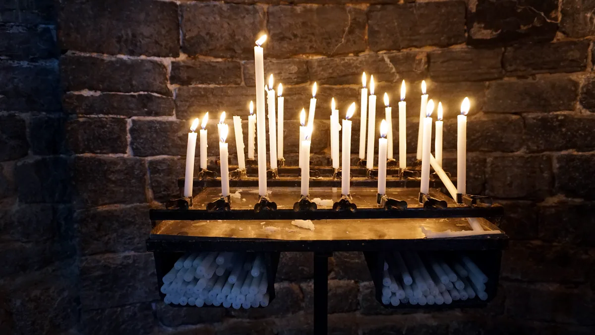 A lit candle standing in a quiet stone church.