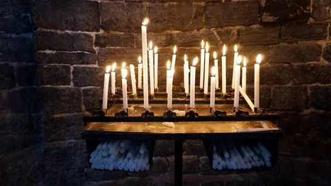 A lit candle standing in a quiet stone church.