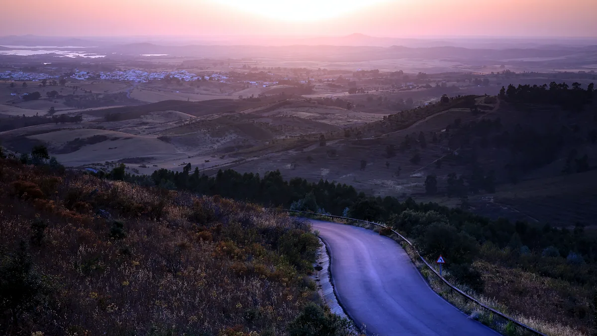 A winding country road under a deep orange sunset sky.