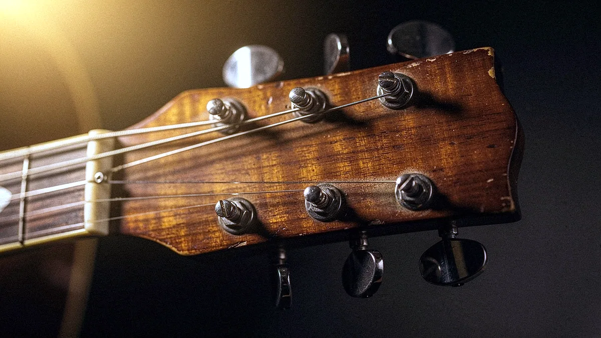 Illustration: The worn headstock and strings of an acoustic guitar in warm light.