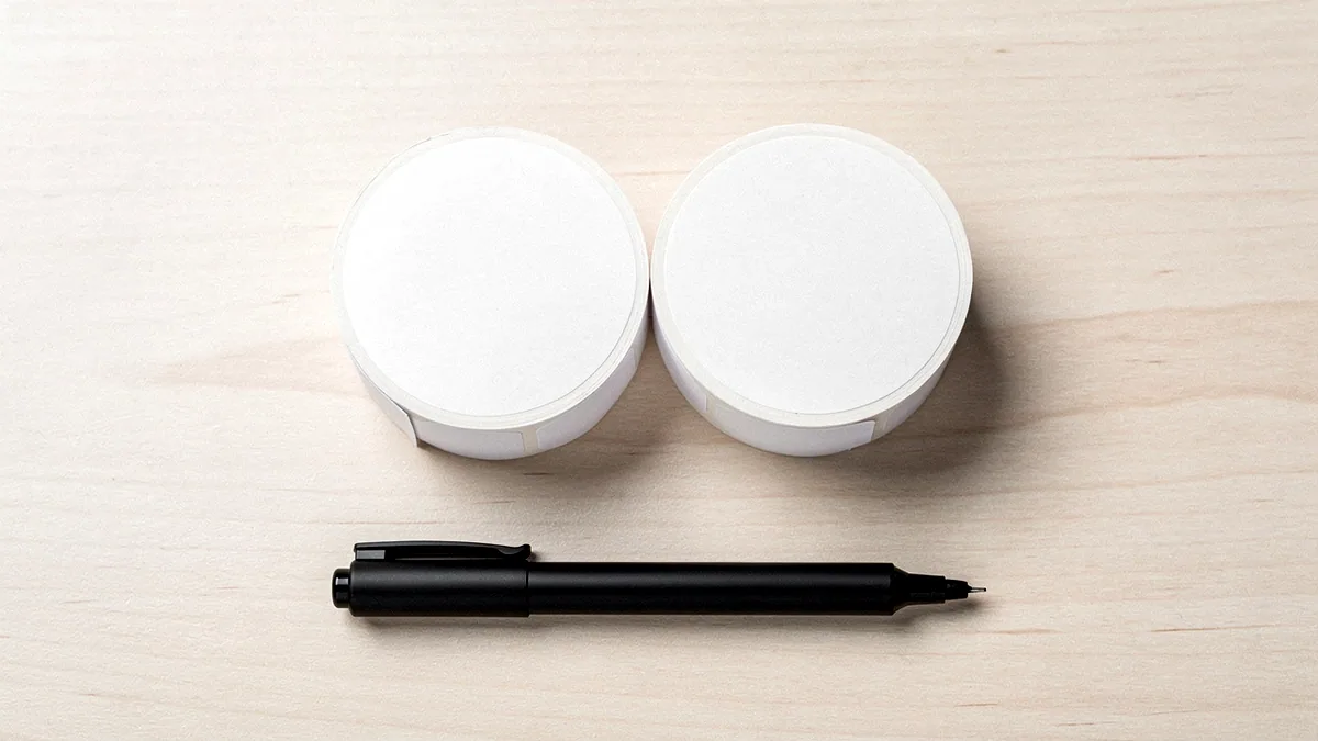 Illustration: Rolls of blank sticker sheets and a marker on a desk.